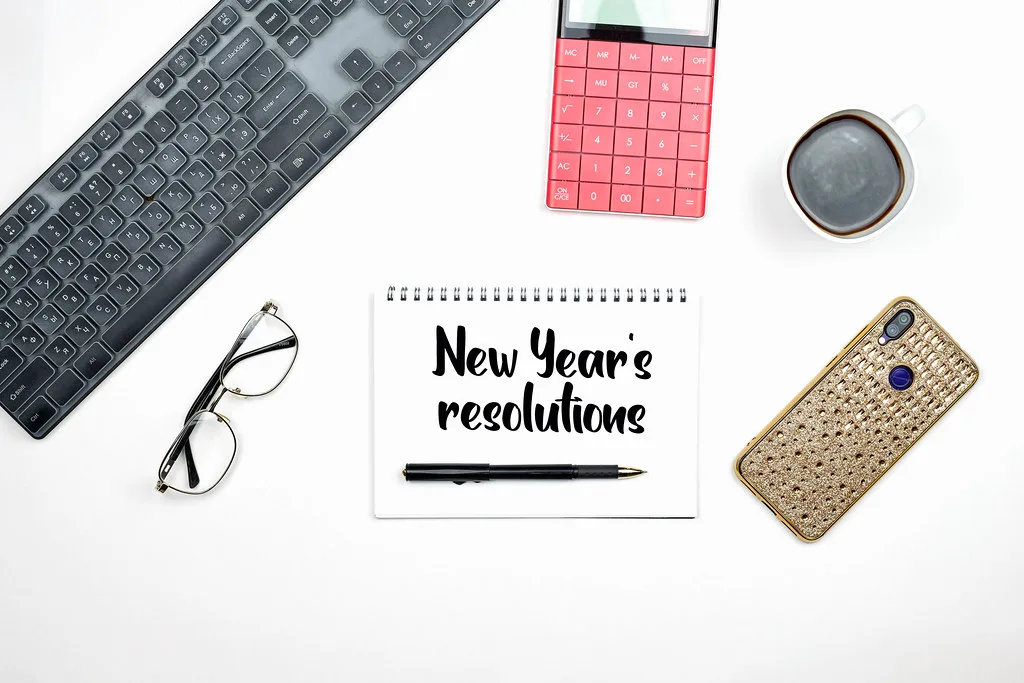 New Year's Resolutions text on notepad with office accessories.
Time to set New Year's Resolutions Goals.