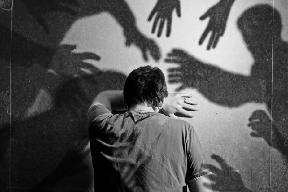 Photo of person with their arm up leaning against a wall with their forehead pressed to their arm. Background has shadows reaching in from all directions towards the person.